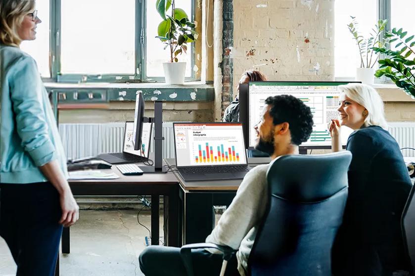 Young professionals in an open floorplan office use LG laptops and monitors as they talk and laugh.