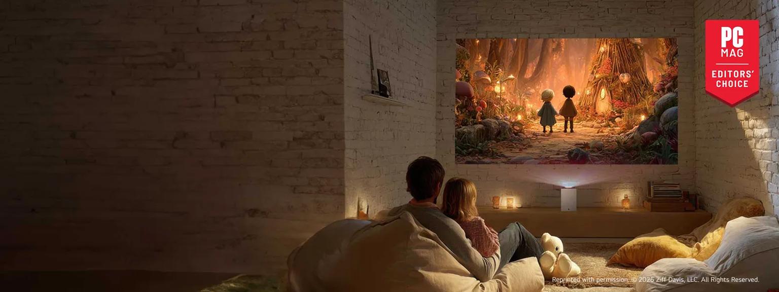 A couple sitting on a couch watching an animated movie projected on a wall by an LG CineBeam S projector in a cozy living room with white exposed brick walls. A red badge reading “PC Mag Editors’ Choice” is in the corner.
