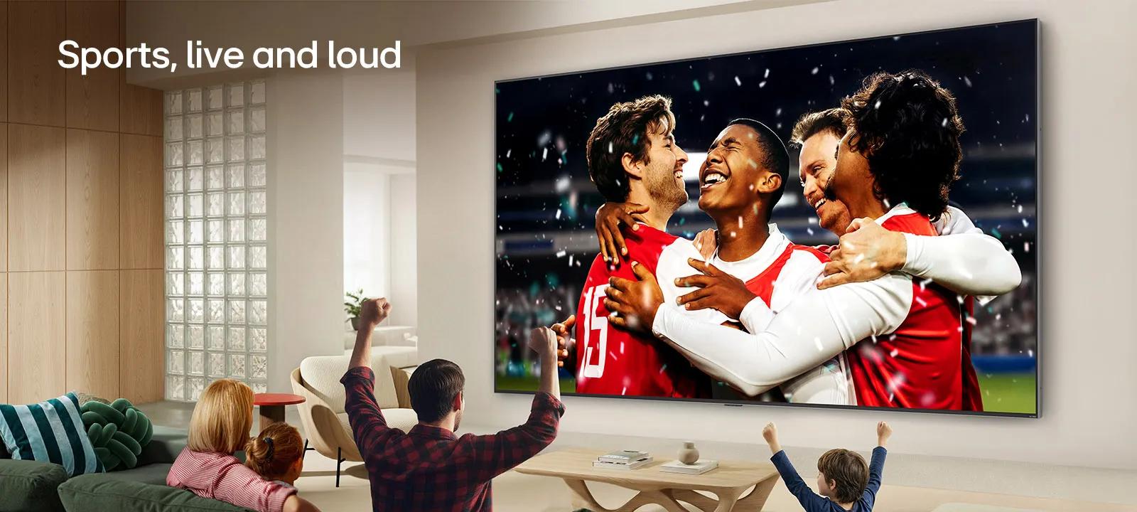 LG Ultra Big TV wall-mounted in a bright living room shows a stadium sports celebration with vivid colors and refined picture quality on a wide screen, while a family seated on sofas cheers together.