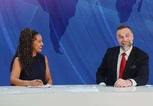 Two newscasters sit at a desk, smiling. Behind them, LG DVLED displays a world map backdrop. 