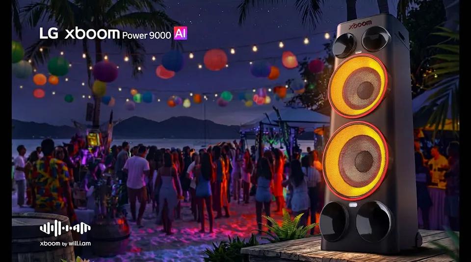 LG xboom Power 9000 AI speaker with glowing orange woofers at an outdoor beach party at night, with colorful lights and a crowd dancing in the background; xboom by will.i.am logo visible in the lower left corner
