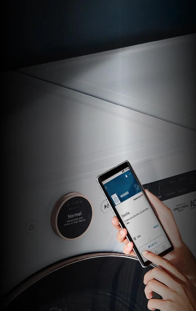Woman standing in front of her washer and try with the ThinQ app on her phone and LG ThinQ logo at the top right.
