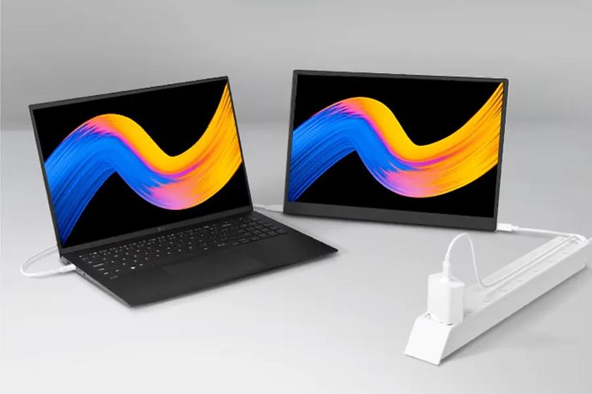 A black laptop and monitor displaying colorful brushstroke graphics, connected by a white cable, with a power strip.
