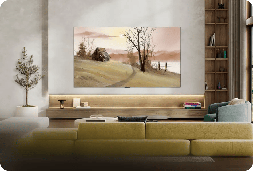 LG OLED TV wall-mounted in a modern living room displaying a Bob Ross-style landscape painting of a rustic cabin at sunrise, with a yellow-green sofa, wooden shelving unit, and potted tree in the foreground