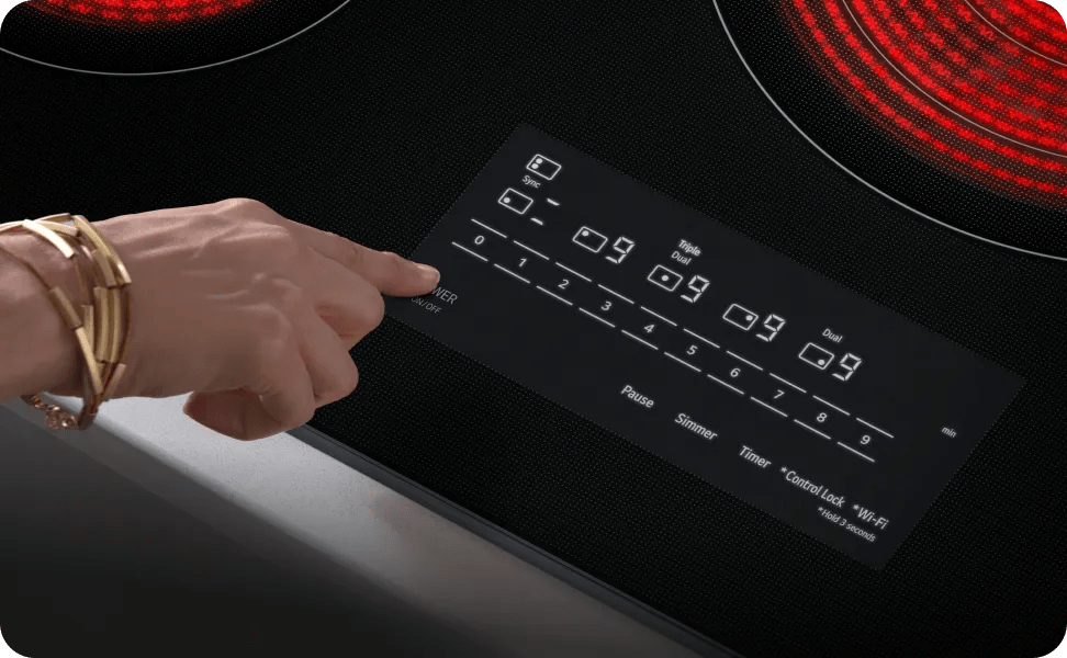 A hand reaches out to touch the ‘Power’ button on the glass controls of an LG electric cooktop.