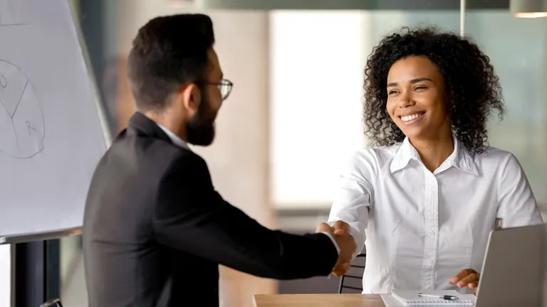 Two people in professional wear smile and shake hands. Near them is an LG gram.