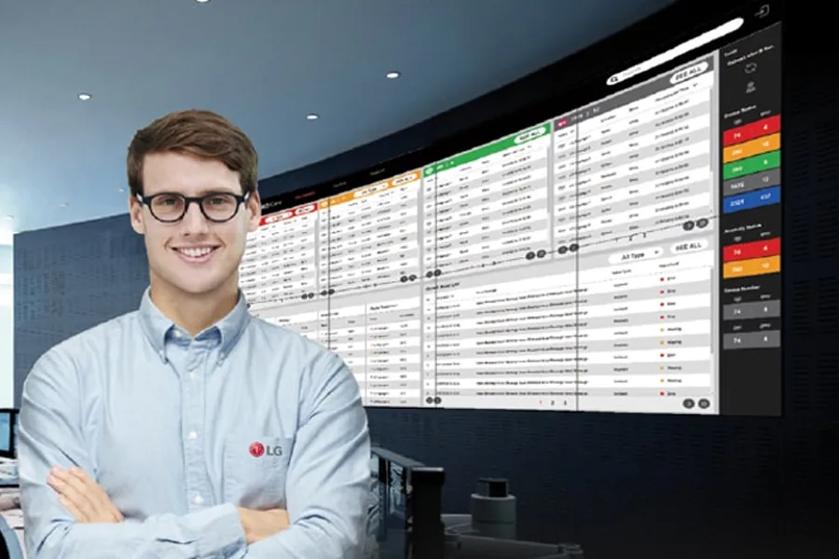 A man in glasses stands in front of a large digital data screen in a control room.