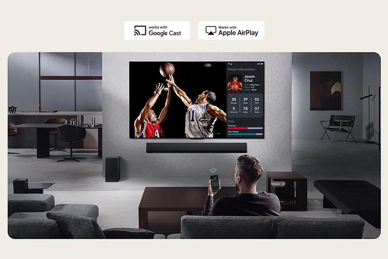 A man sits in a modern living room and uses the ThinQ™ app on his phone to split the QNED TV into multiple views.