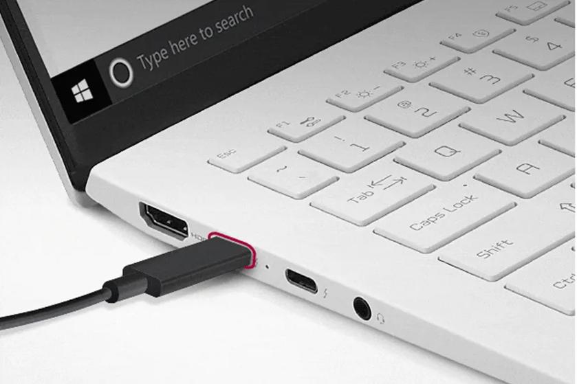 Close-up of a white laptop's right keyboard section with USB-C port, a black cable plugged in, and visible screen search bar.