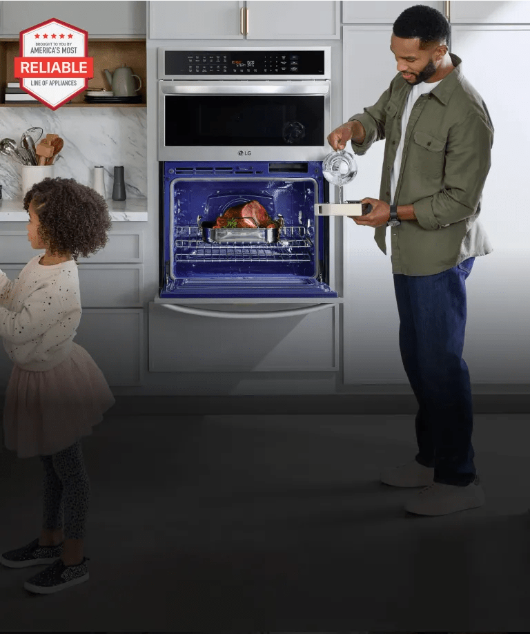 A mother slicing oranges for her daughter at the kitchen island while the father cooks a ham in their LG wall oven - tablet