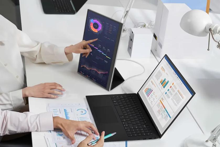 Two people analyzing data on a laptop and vertical monitor at a white desk.