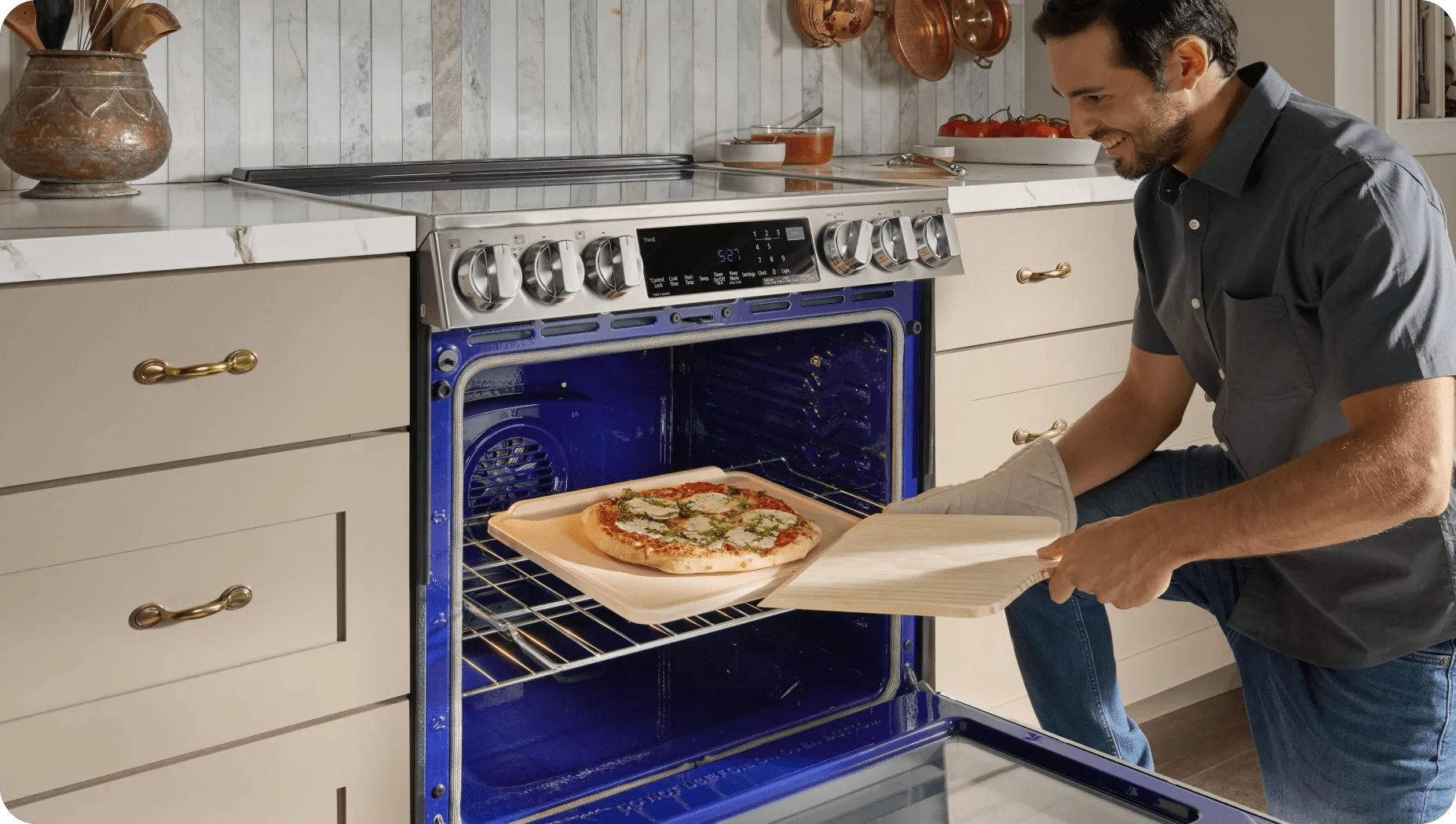 A man takes a cooked pizza off an oven rack from an LG oven in a brightly lit modern kitchen.