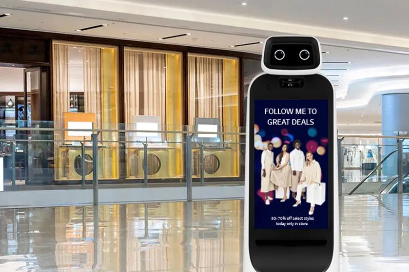 CLOi stands in an upscale shopping mall or department store. Her display shows a fashion graphic with the words 'follow me to great deals' above it.