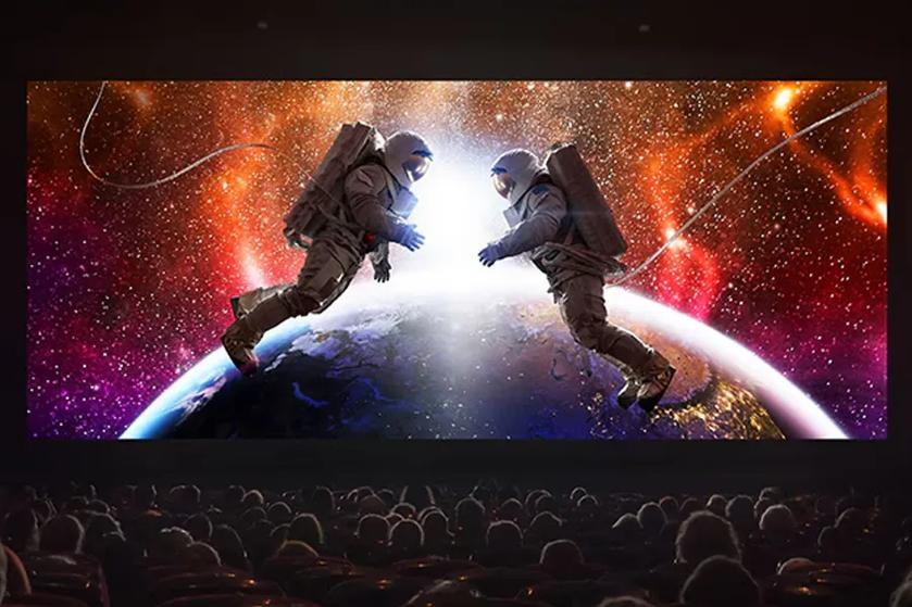 Astronauts in space above Earth on a movie screen with a theater audience.