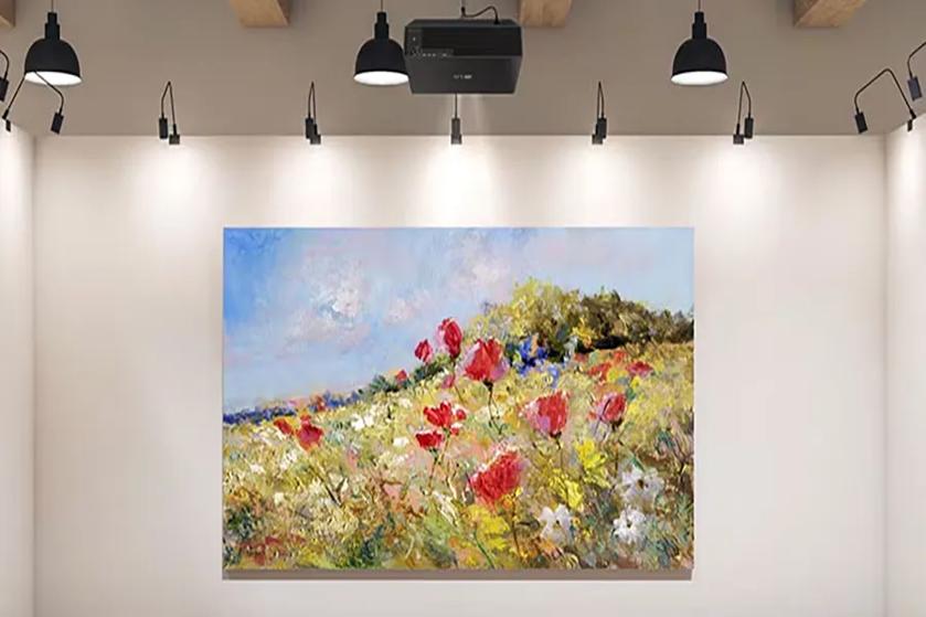 A painting of a colorful wildflower field under a blue sky, illuminated by spotlights in a gallery.