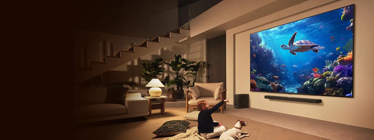 A child sits next to a dog and points at an LG QNED evo screen with an image of a swimming sea turtle on it.