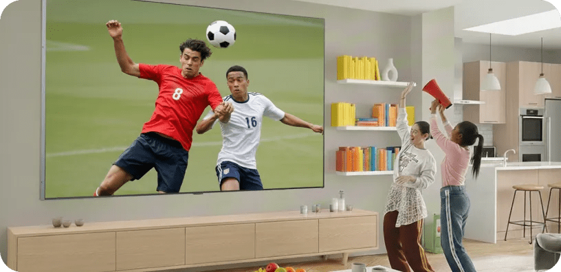 LG Ultra-Large TV mounted above a console showing a live soccer match, while a family in a bright, casual living room cheers and celebrates.