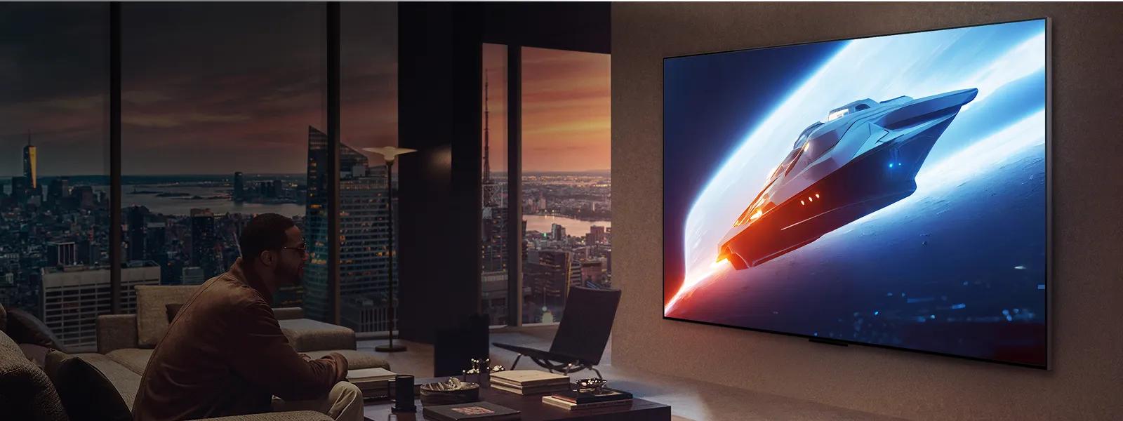 Man in modern apartment watches a wall-mounted TV showing a spaceship, with city skyline visible through large windows at dusk.