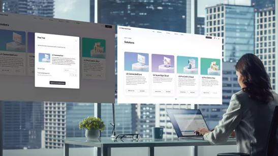 A businesswoman sits at her desk, using a laptop to access LG software. Two large floating screens above her further showcase what she's looking at, displaying the LG Business Cloud software solutions pages of the LG website.