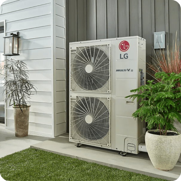 LG MULTI V outdoor HVAC unit with dual fans installed on a modern home exterior, positioned between vertical and horizontal siding panels, flanked by decorative potted plants and a wall-mounted lantern, next to a patch of green grass.