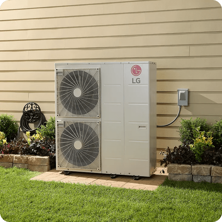 Large LG HVAC outdoor unit with dual fans installed against the beige siding of a house, surrounded by a neatly landscaped garden with green grass, flowers, and shrubs.
