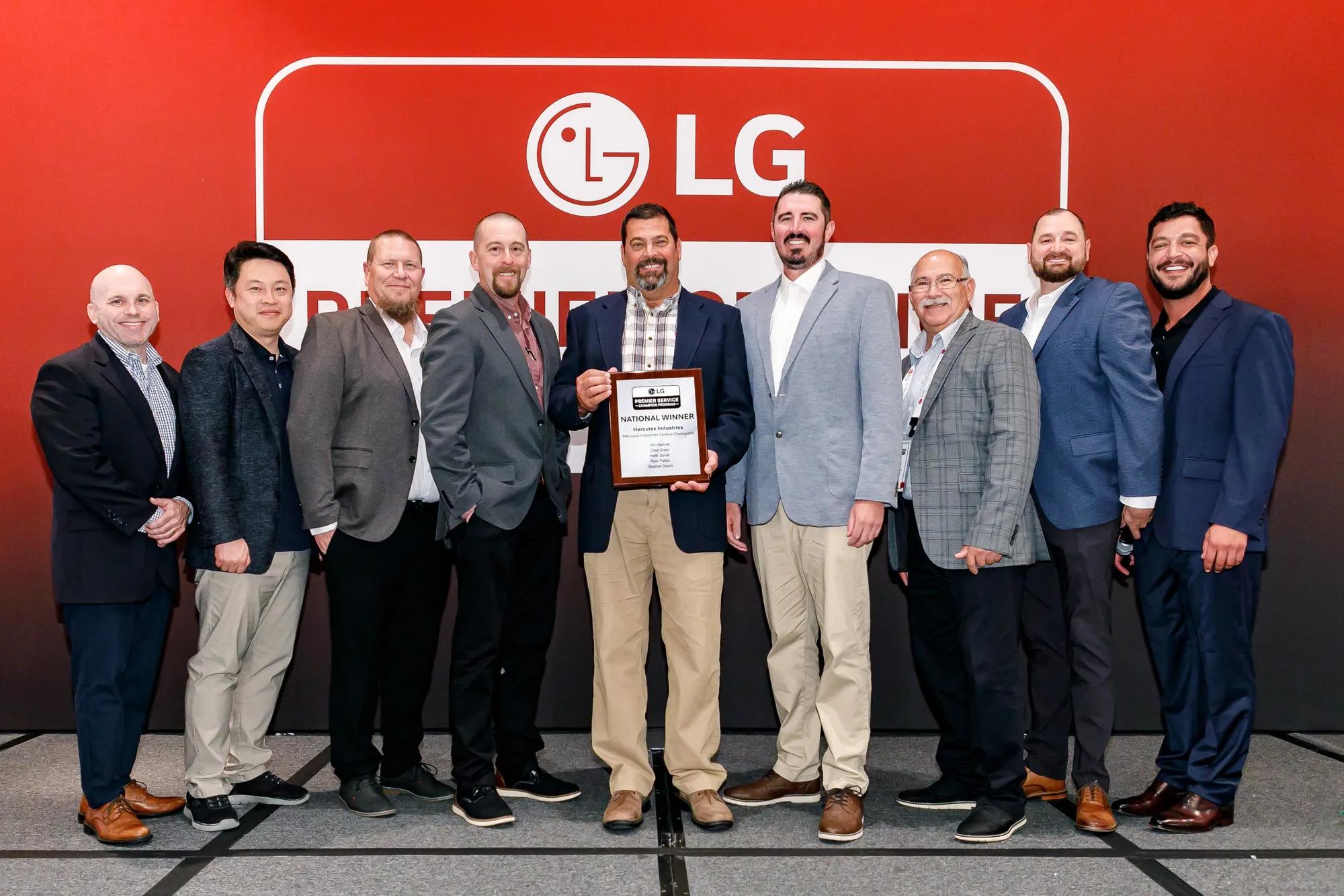 Nine men in sport coats stand in front of a red LG backdrop, and the man in the center holds an LG Premier Service Champion Program National Winner plaque awarded to Hercules Industries.