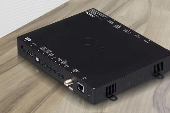 An LG Pro:Centric Set Top Box sitting on a wooden surface, with a background of wavy white abstract lines behind it. 