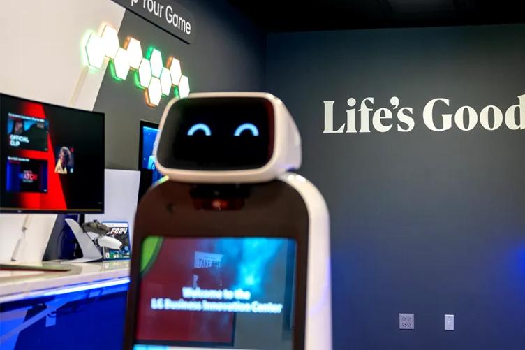 LG CLOi GuideBot with a cheerful expression on her robotic face display. Behind her is a display area full of LG gaming monitors, and the slogan Life's Good on the wall. 
