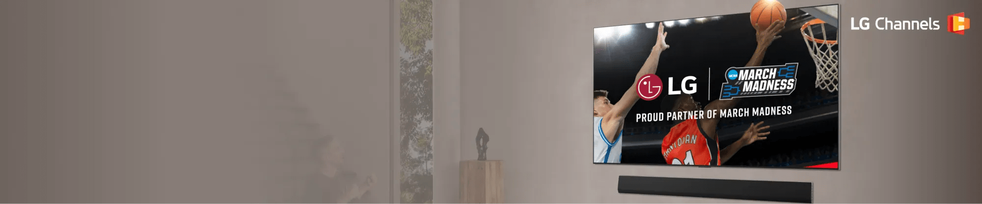 An LG TV mounted on a wall displays a close-up of a basketball player in a red jersey performing a layup being challenged by a player in a white jersey as a fan cheers on in a modern living room. Partnership lockup of LG and NCAA March Madness is overlayed on the TV.