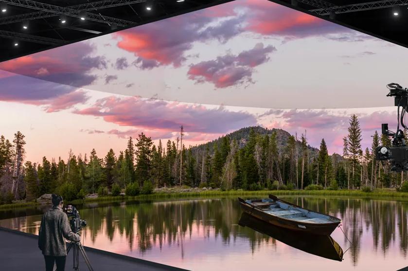 A cameraman readies his shot in the studio. Before him, LG Studio Series for walls, ceiling, and floor create a compelling scene featuring a mountain lake at sunrise.