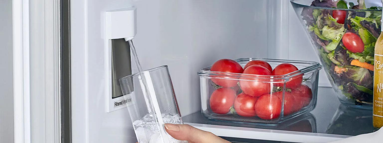 Hand holing glass being filled by internal refrigerator water dispenser.