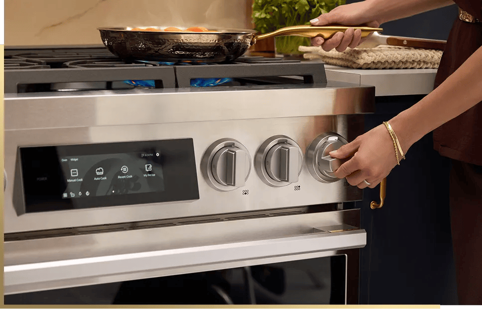 LG SIGNATURE gas range with touchscreen display showing Manual Cook, Auto Cook, Recent Cook, and My Recipe options, person adjusting control knob while cooking on active burners