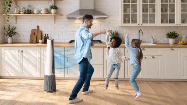 LG tower air purifier with blue airflow graphic in a bright kitchen as a father and two children dance nearby