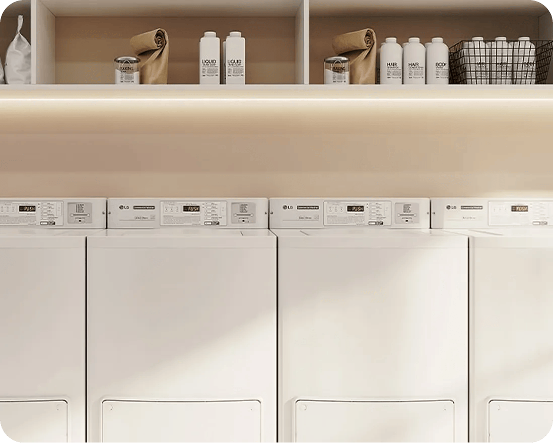 Row of LG commercial laundry machines with control panels, shelving above holding detergent bottles and supplies.