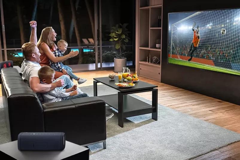 A family sitting on a couch watching soccer on TV with sound connected on LG Xboom Speakers making QNED the best tv for sports