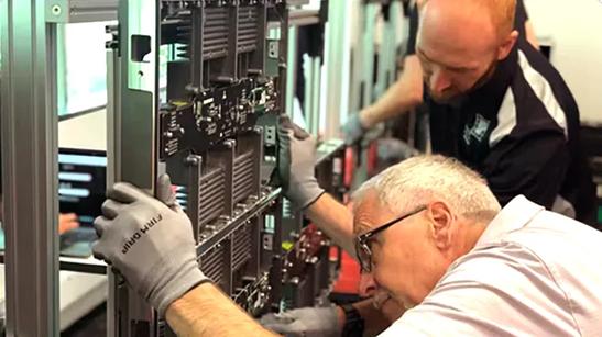 Two men with work gloves handle an LG display panel as they learn about and are trained on Direct View LED and other LG products.