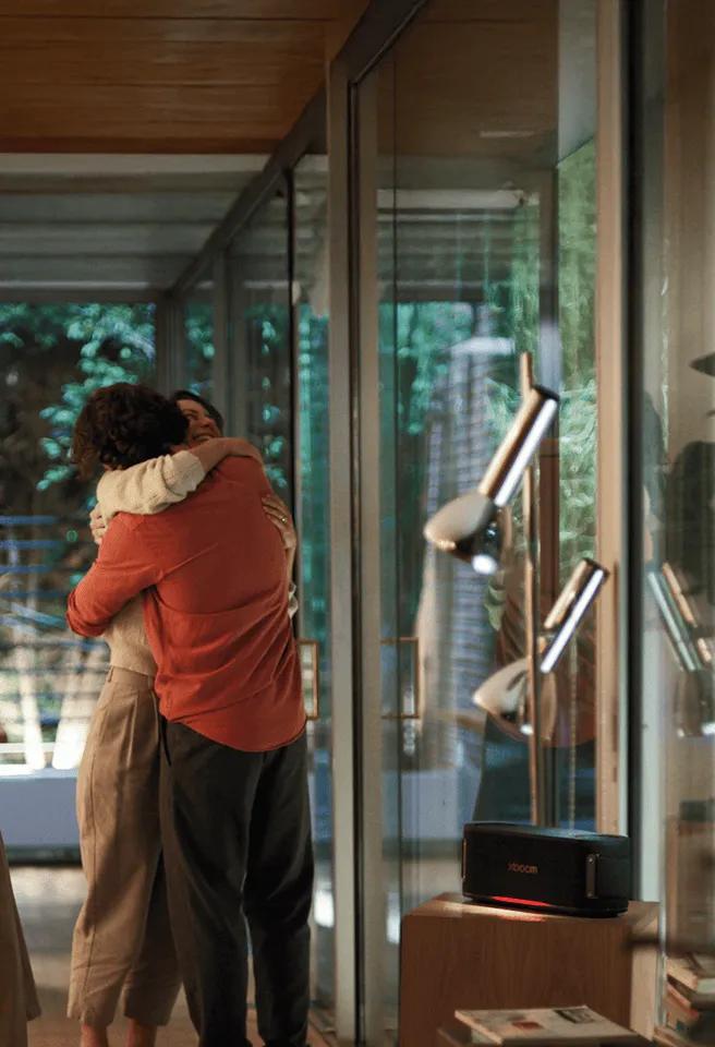 A woman and a man embrace in the living room, with the XBOOM speaker turned on beside them.