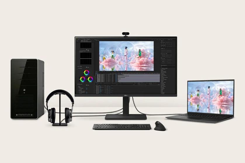 The image shows a computer workstation setup on a light beige background. At the center is a large flat-screen monitor displaying a colorful image editing interface with three individuals standing among clouds and reflections. To the left of the monitor is a black desktop computer tower with a glossy front panel. A pair of over-ear headphones rests on a stand between the computer tower and the monitor. A keyboard and mouse are placed directly in front of the monitor, on the desk surface. To the right of the central monitor, a slim laptop displays the same image on its screen, showing a seamless extension of the digital workspace. Cables are visibly connecting the devices.