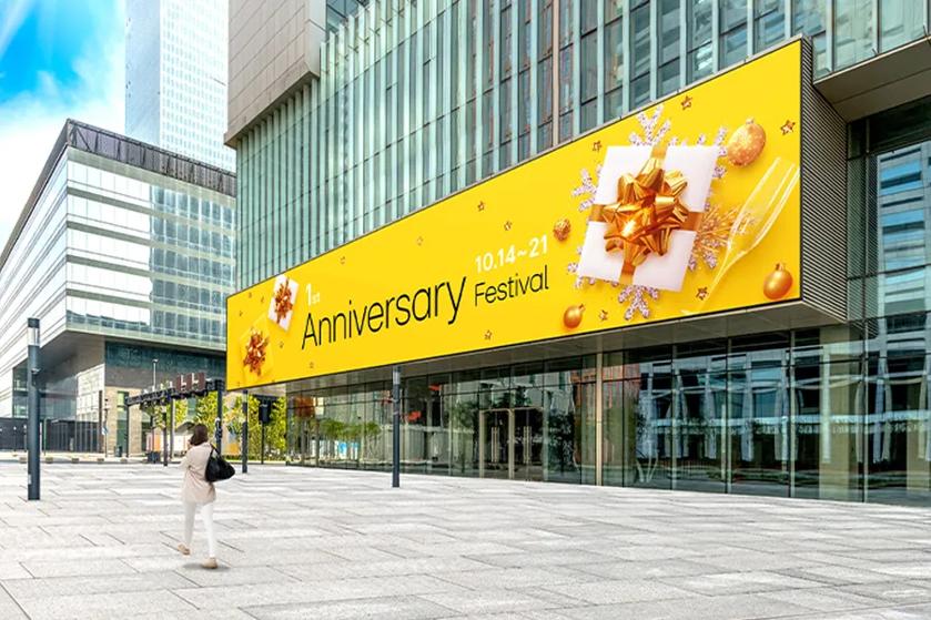 A large yellow billboard on a modern glass building advertising a festival with festive decorations.