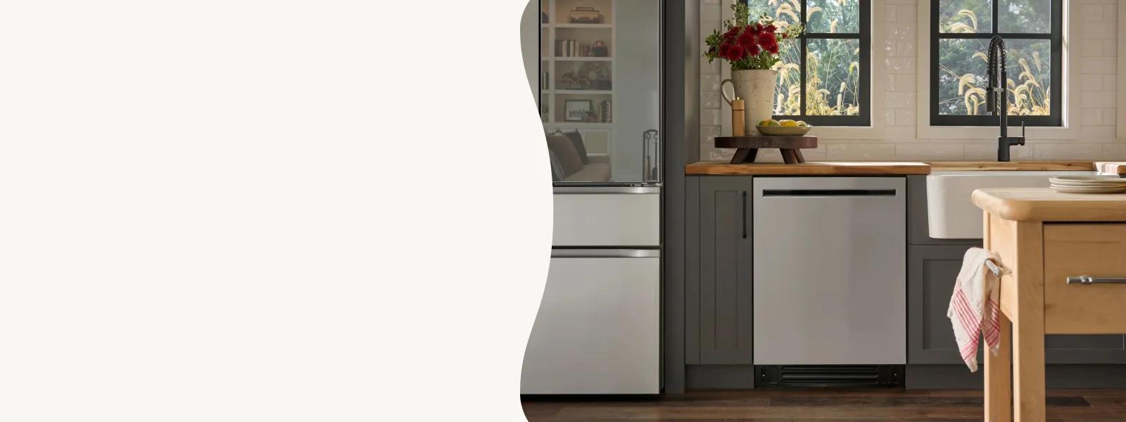 A contemporary kitchen displays a flush-fit LG dishwasher integrated into dark grey cabinetry with butcher block countertops. The bright space includes three large windows overlooking a garden, a wooden kitchen island on wheels, and dark hardwood flooring.