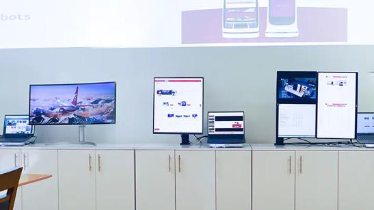 Several LG monitors including ergonomic monitor and curved monitor on a white display shelf, with various wallpapers and websites on their screens, on display at the LG Atlanta Business Innovation Center.