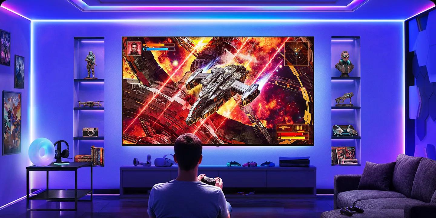 LG TV with clutter-free setup shows a wall-mounted TV in a gaming room, where minimal visible cables create a clean environment as a player faces the screen, illustrating a streamlined and flexible wireless gaming setup.
