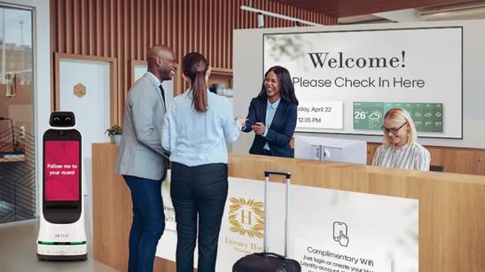 A couple check into a hotel with friendly receptionists, bold LG signage, and LG CLOi GuideBot waiting to escort them to their room.