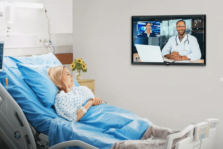 A patient reclining in a hospital bed watches the news on an LG Pro:Centric Hospital TV. 