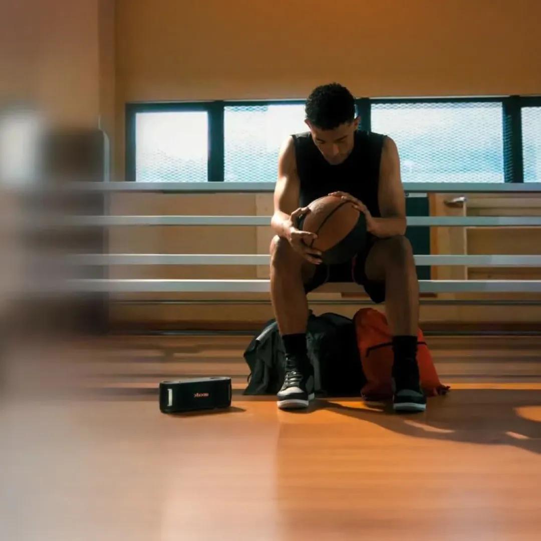 A man takes a break from basketball with his xboom speaker beside him.
