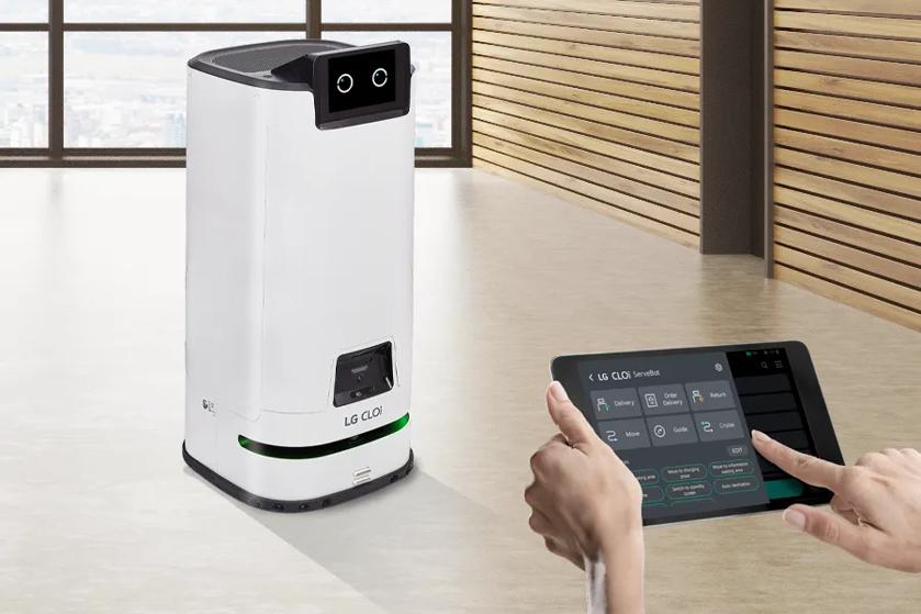 CLOi ServeBot driving down a hallway. In the bottom left, a pair of hands uses a tablet to remotely manage her route.