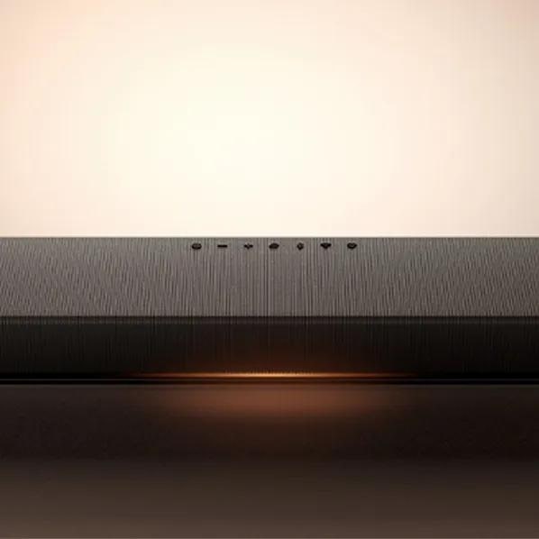 Image of an LG Sound Suite H7 soundbar with a warm glow beneath it, emphasizing its sleek control panel and streamlined design.