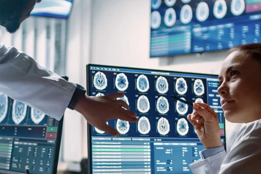 A doctor sitting in a medical office. Before her is an LG medical monitor with brain scans and medical information. She's looking at a colleague who is mostly out of frame, only their arm visible. The colleague is pointing to information on the medical display. 