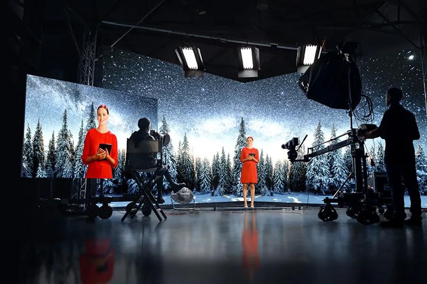 A studio setting with a woman in a red dress against a snowy, starry backdrop, surrounded by cameras and lighting equipment.