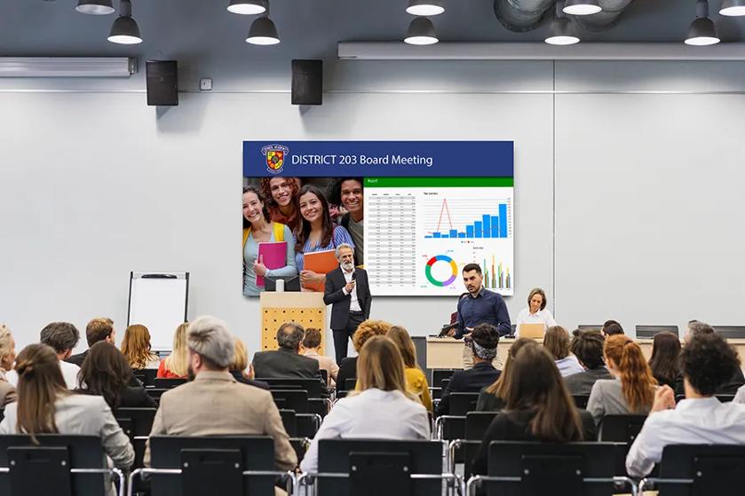 A school board meeting with a large LG display behind the speaker.